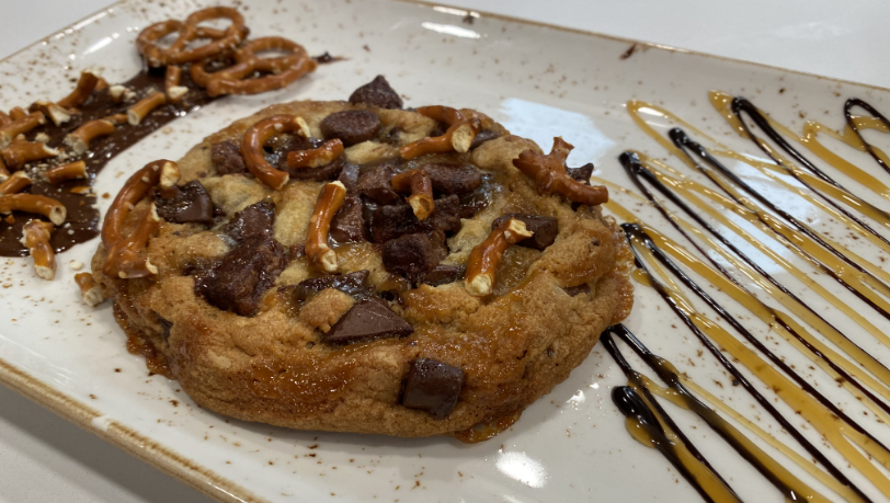 Freshly baked chocolate cookie with pretzels ontop and chocolate and caramel drizzle. 