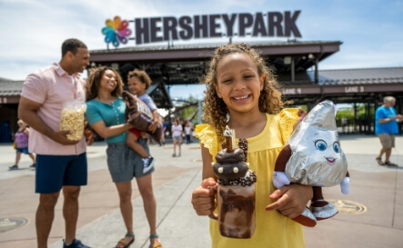 Family in front of Hersheypark front gate along with girl holding dessert